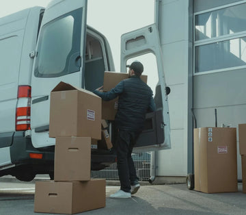 Person unloading cardboard boxes from a van outside a building